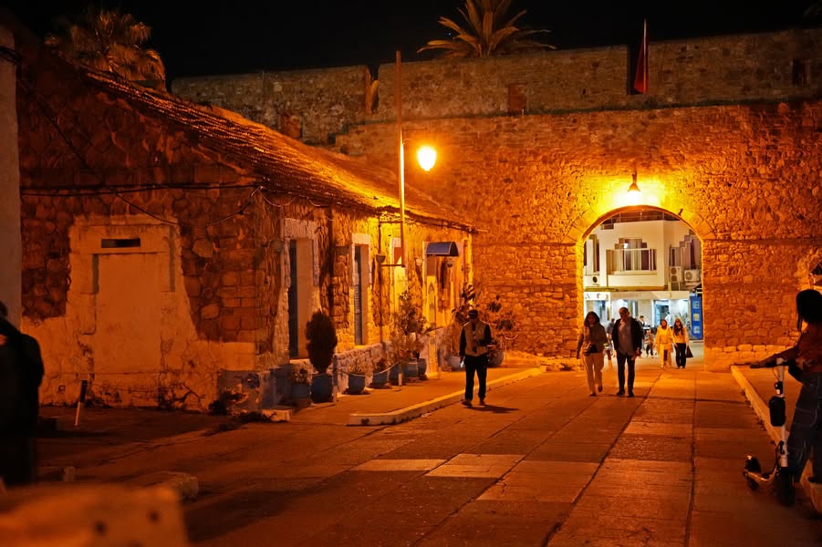 The gate. It watches. Centuries pass through its mouth, dragging…